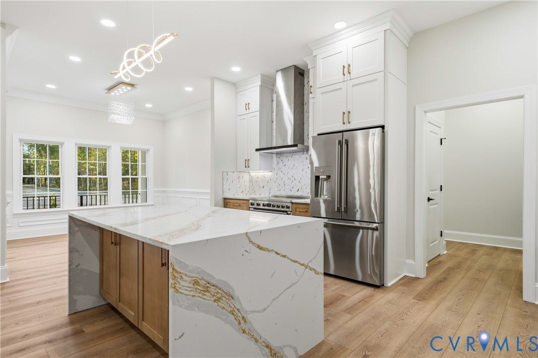 Kitchen featuring a central island with a waterfall-edge countertop, floor-to-ceiling white cabinetry, stainless steel appliances, and wood-finish flooring