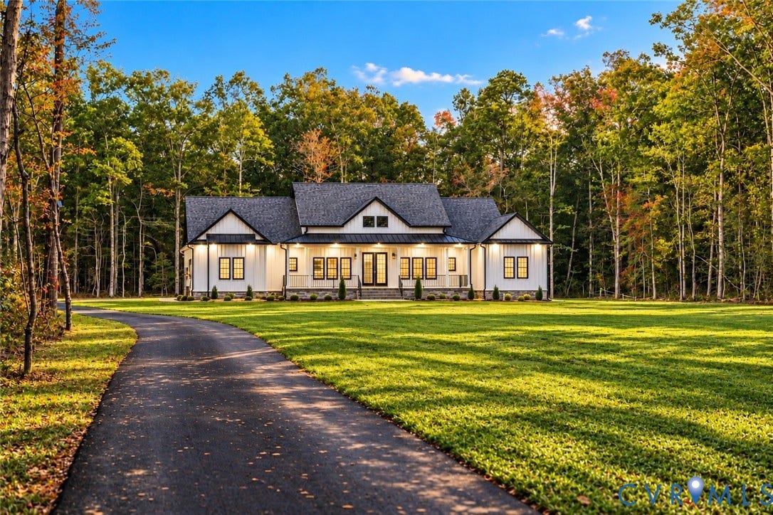 Modern farmhouse exterior featuring vertical siding, a covered front porch, stone foundation detailing, a gabled roofline, and an asphalt driveway