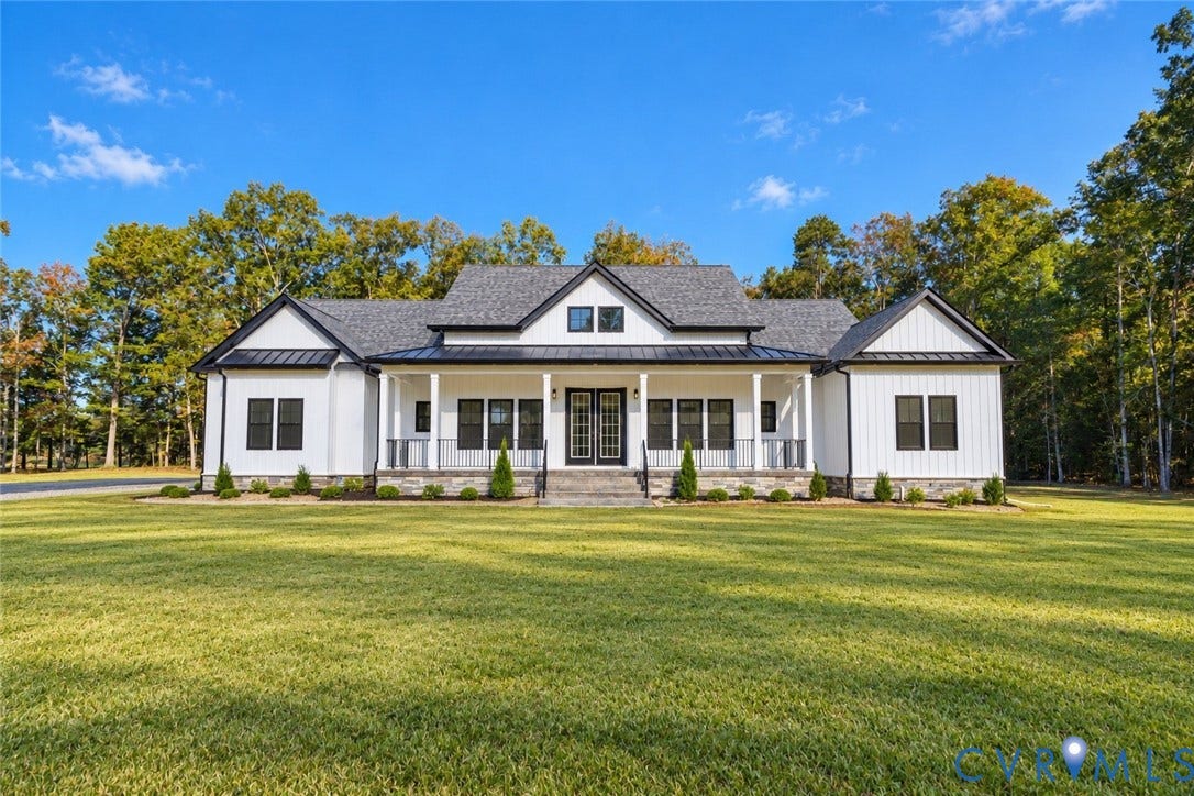 Farmhouse-style exterior featuring vertical board-and-batten siding, a covered front porch with dark metal roofing, black-framed windows, and stone masonry foundation trim