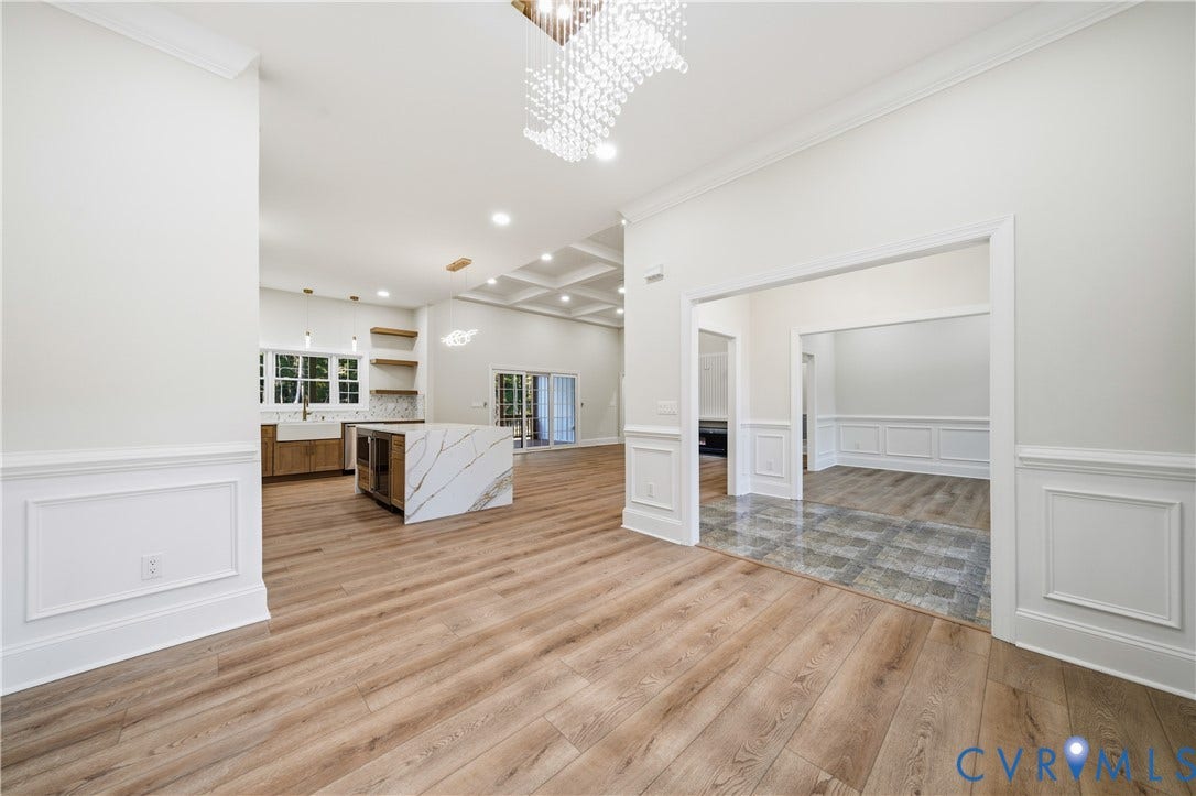 Interior space featuring wood-finish flooring, wainscoting, coffered ceilings, a quartz-topped kitchen island, and crystal chandelier lighting