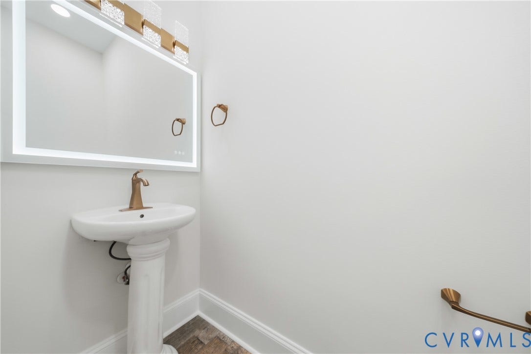 Pedestal sink with a brass-finish faucet, illuminated rectangular mirror, decorative metallic light fixture, and brass-finish hardware