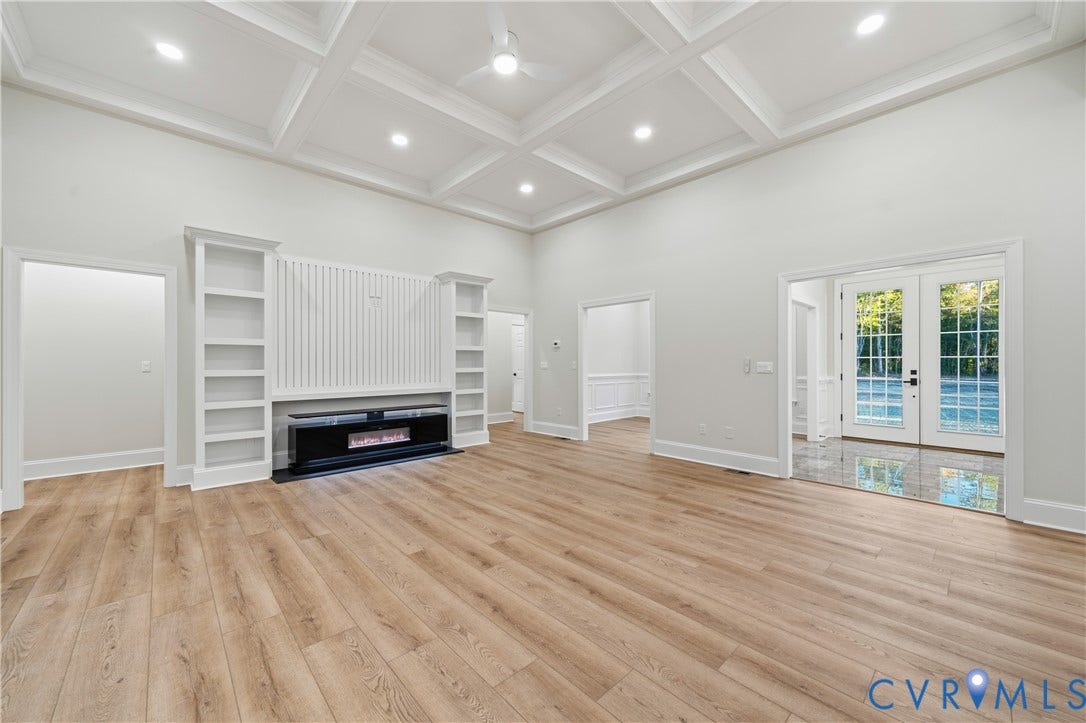 Living space featuring a coffered ceiling, wood-finish flooring, built-in cabinetry surrounding a fireplace, and double glass-paneled doors