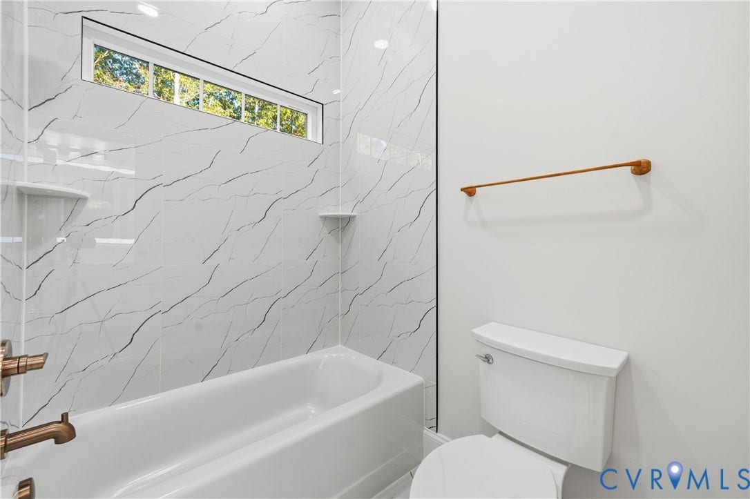 Full-height tub enclosure with patterned wall tile, transom window, built-in corner shelving, and metallic fixtures