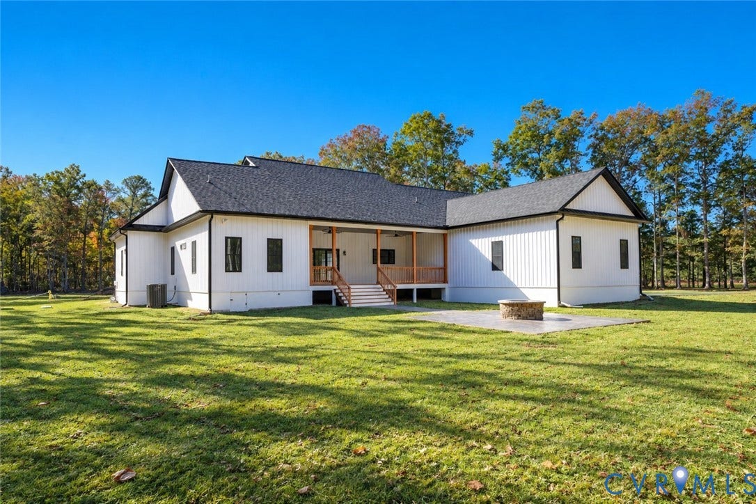 Modern farmhouse exterior featuring vertical siding, a covered rear porch, a stone-accented fire pit, and expansive grounds
