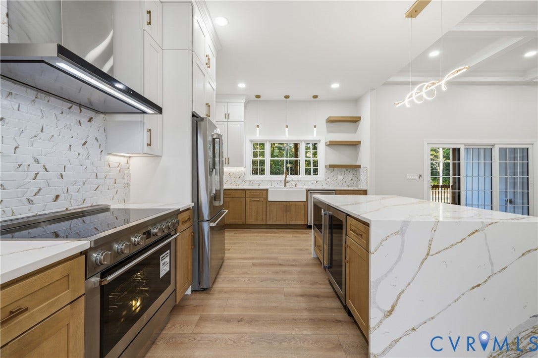 Kitchen featuring custom wood-finish cabinetry, a waterfall-edge island with stone-finish countertop, apron-front sink, stainless steel professional-grade range, and patterned tile backsplash