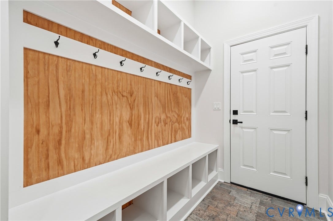 Custom built-in storage featuring a wood-panel accent wall, integrated cubbies, matte black hooks, and a white finish bench, paired with a six-panel door and stone-finish tile flooring