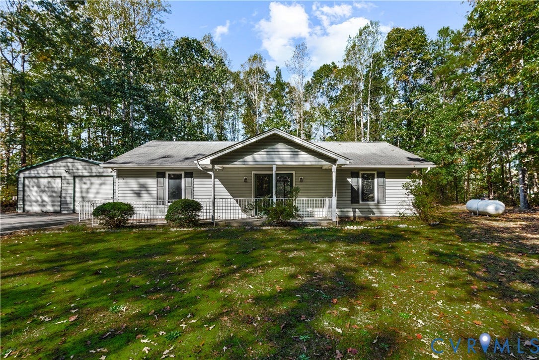 20040 Paradise Lane, Ruther Glen, VA 22546 Single-story residence featuring vinyl siding, a covered front porch, a detached two-car garage, and mature tree-lined grounds