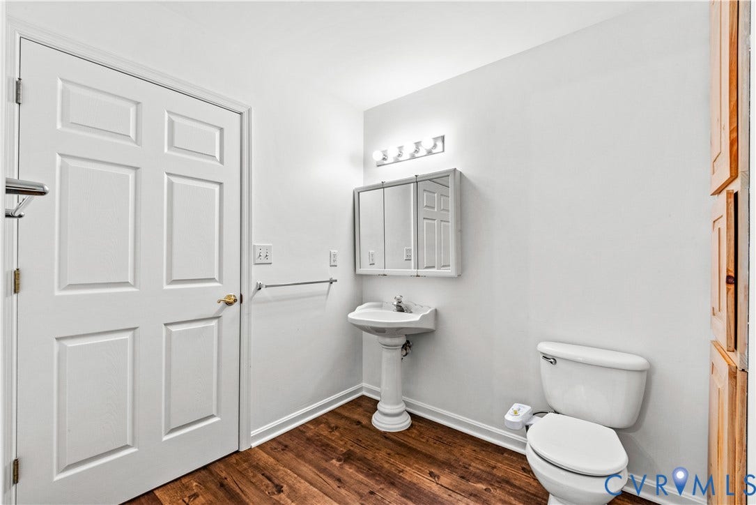20040 Paradise Lane, Ruther Glen, VA 22546 Bathroom featuring wood-finish flooring, a white pedestal sink, a multi-panel mirrored medicine cabinet, a four-light fixture, and built-in wood cabinetry