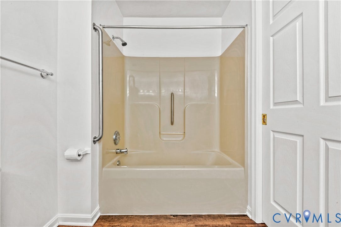 20040 Paradise Lane, Ruther Glen, VA 22546 Tub and shower combination with an integrated surround, metallic wall-mounted grab bars, wood-finish flooring, and a multi-panel door with gold-tone hardware