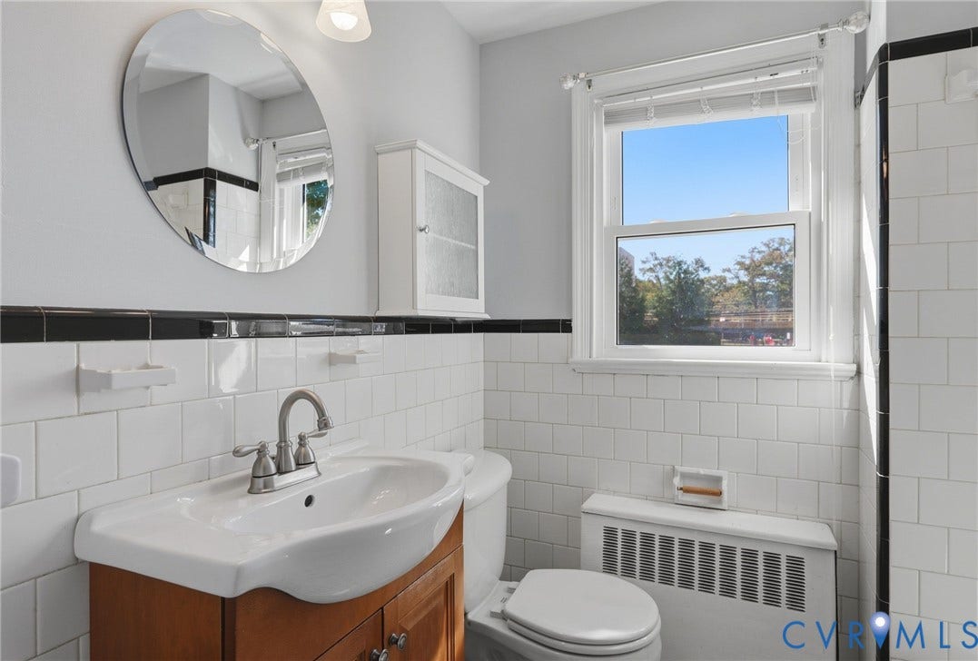 5028 Devonshire Road, Richmond, VA 23225 Bathroom featuring a white subway tile surround with black accent tiling, a wood-finish vanity with a drop-in sink, a circular wall-mounted mirror, and a wall-mounted medicine cabinet