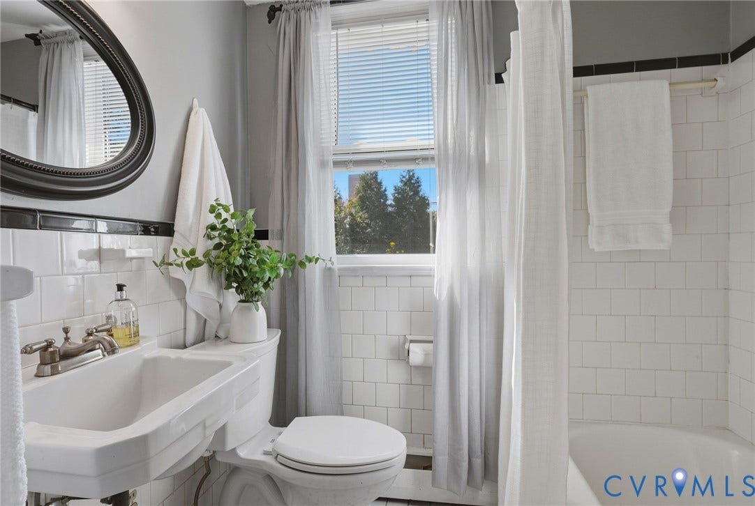 5028 Devonshire Road, Richmond, VA 23225 Wall-mounted porcelain sink with metallic dual-handle faucet, oval-framed mirror, white subway tile wall surround, and deep soaking tub