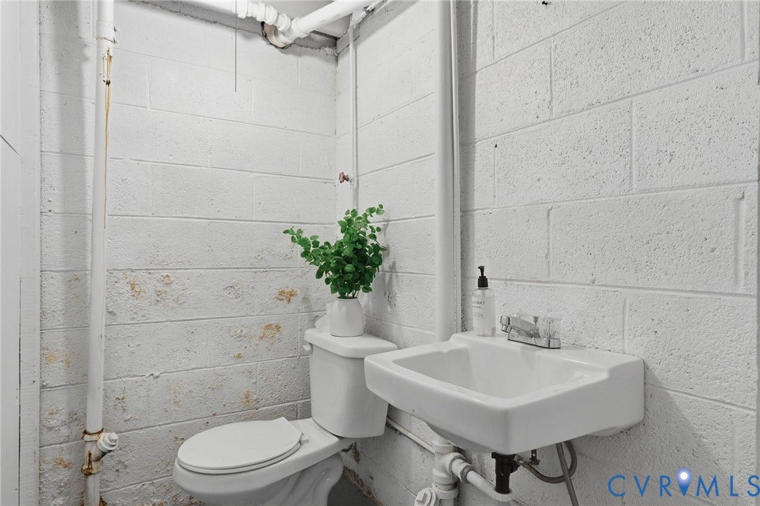 5028 Devonshire Road, Richmond, VA 23225 White painted masonry walls featuring a wall-mounted vitreous china sink with a dual-handle chrome faucet and a standard porcelain toilet