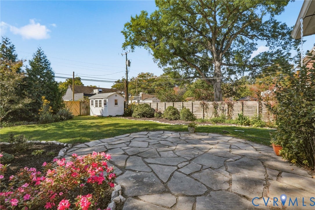 5028 Devonshire Road, Richmond, VA 23225 Backyard featuring a flagstone patio, manicured lawn, detached storage structure, mature trees, and perennial garden beds