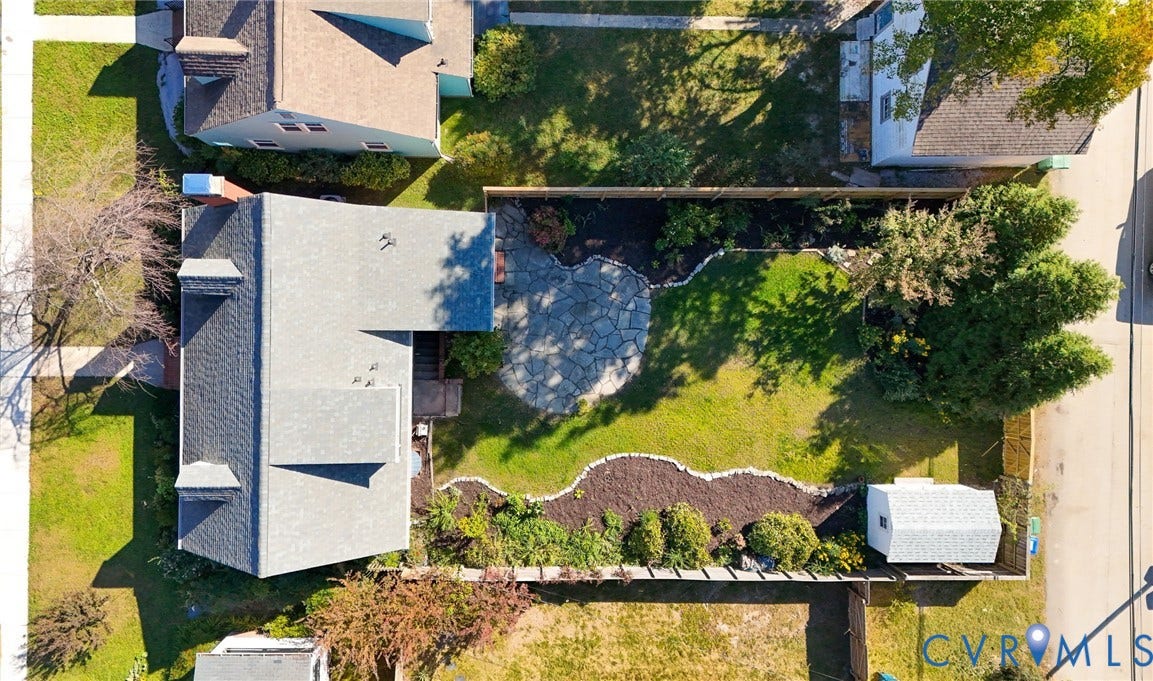 5028 Devonshire Road, Richmond, VA 23225 Aerial view of a rear yard featuring a stone patio, manicured lawn, perimeter landscaping beds, and a detached storage structure enclosed by fencing