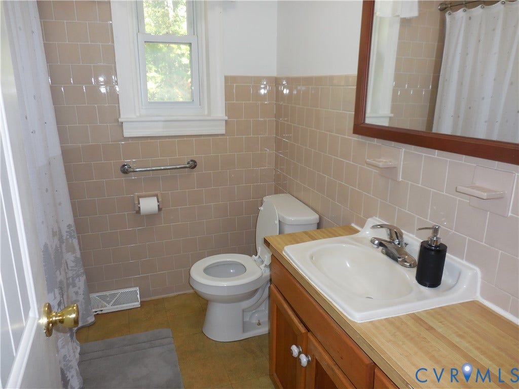 25 Bethany Church Road, Bumpass, VA 23024 Bathroom featuring tan ceramic wall tile, wood-finish cabinetry, inset sink with metal hardware, and a framed mirror