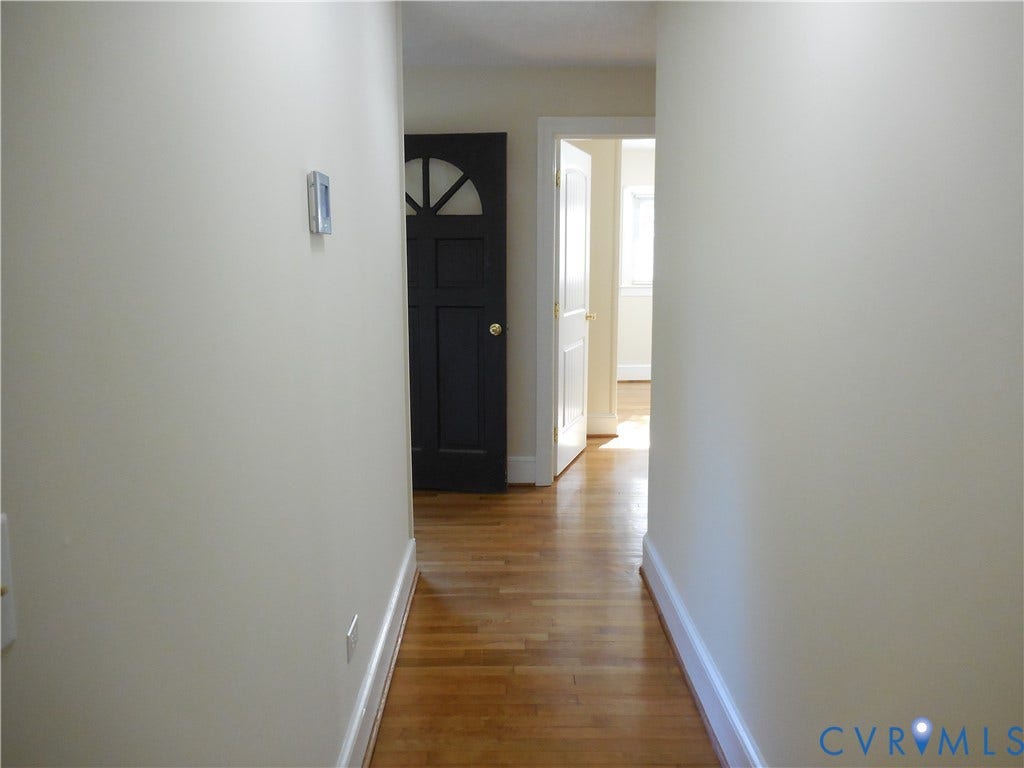 25 Bethany Church Road, Bumpass, VA 23024 Hallway featuring wood-finish flooring, a dark-toned door with a semi-circle window inlay, and white painted interior doors with traditional millwork