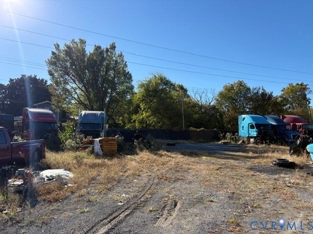 1143 McKenzie Street, Petersburg, VA 23803 Expansive exterior lot featuring a stabilized gravel surface, mature tree line, and perimeter mesh fencing