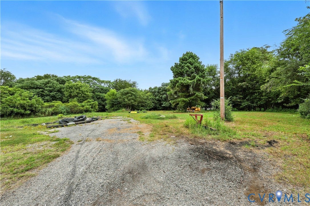 1143 McKenzie Street, Petersburg, VA 23803 Expansive lot featuring gravel-surfaced drive area, open grassy terrain, and mature perimeter trees