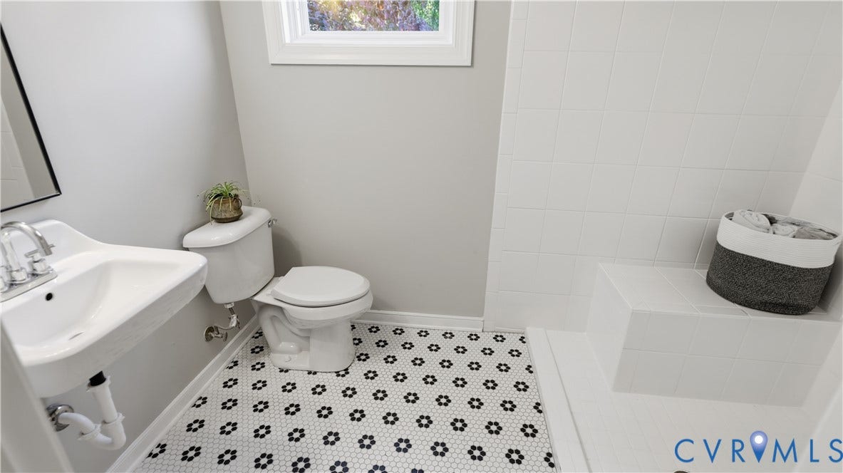 10010 Cheyenne Court, Richmond, VA 23235 Bathroom featuring a wall-mounted sink with chrome faucet, hexagonal patterned floor tile, white square-tiled shower surround, and built-in shower bench