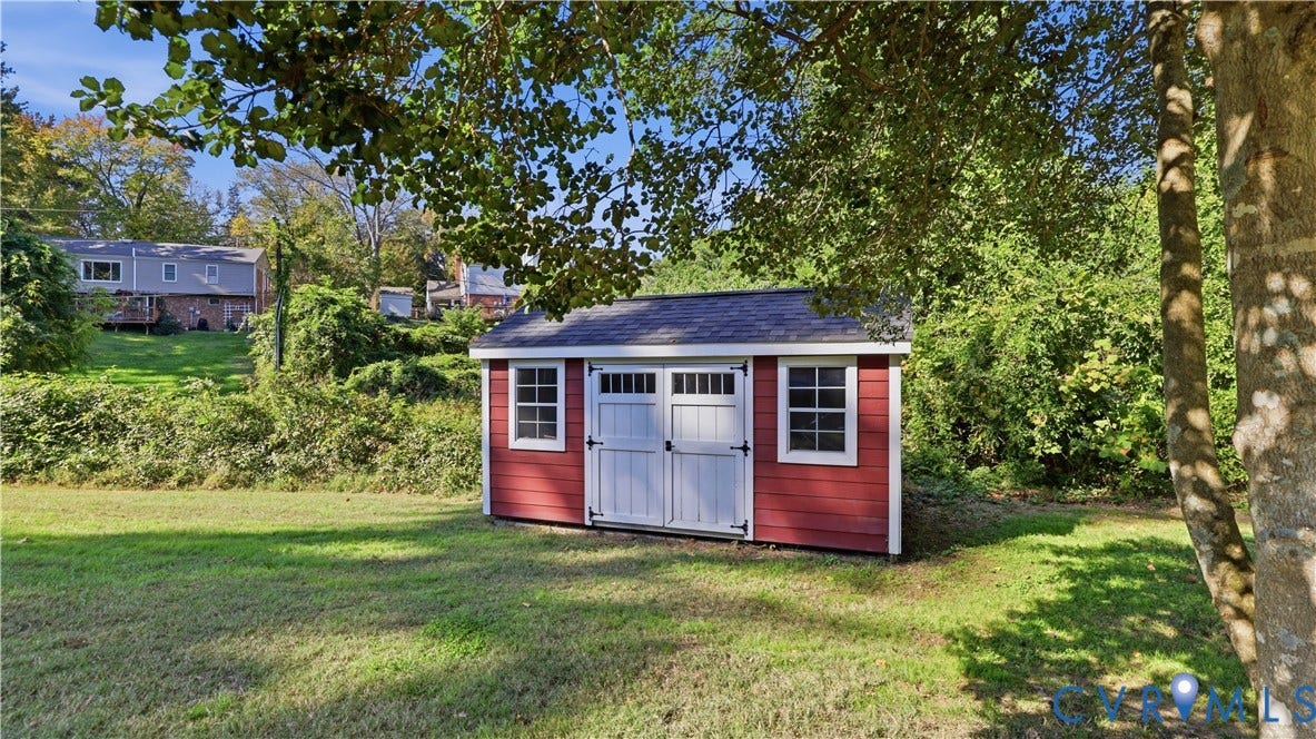 10010 Cheyenne Court, Richmond, VA 23235 Exterior storage structure with a red wood-sided facade, asphalt shingle roof, double-entry doors, and window accents situated on a grass-covered lot