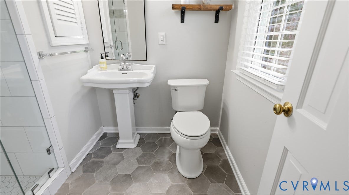 10010 Cheyenne Court, Richmond, VA 23235 Bathroom featuring a white pedestal sink, glass-enclosed shower with white subway tiling, grey hexagonal floor tile, and a wall-mounted wooden shelf
