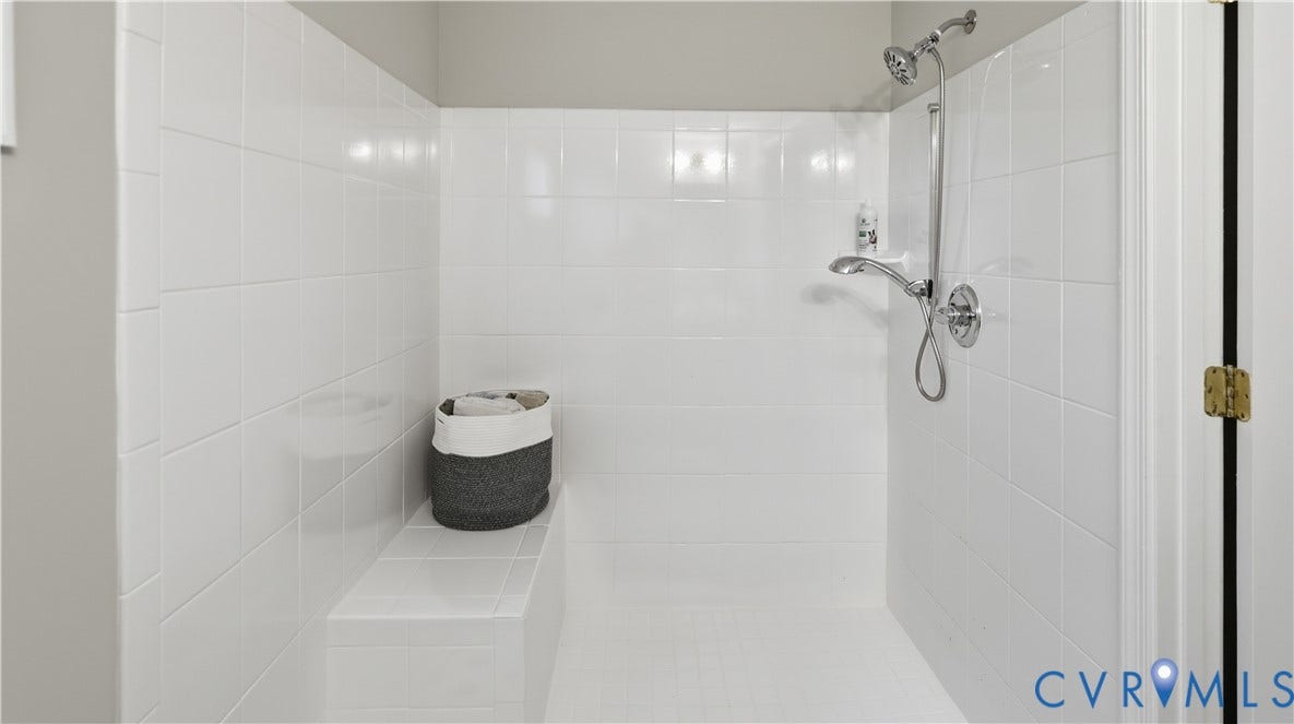 10010 Cheyenne Court, Richmond, VA 23235 Walk-in shower enclosure featuring white wall tiling, integrated tile bench, and chrome hardware including a detachable showerhead