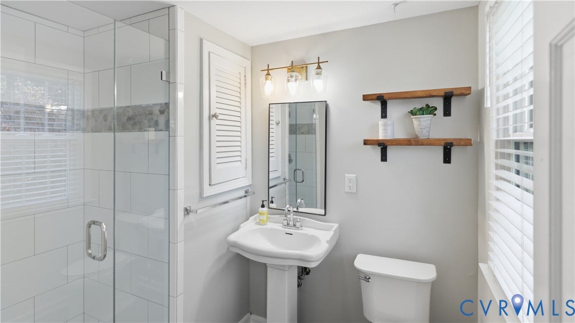 10010 Cheyenne Court, Richmond, VA 23235 Bathroom featuring a walk-in shower with glass enclosure, white subway tile surround, pedestal sink, wall-mounted shutter-style cabinetry, and a three-light vanity fixture