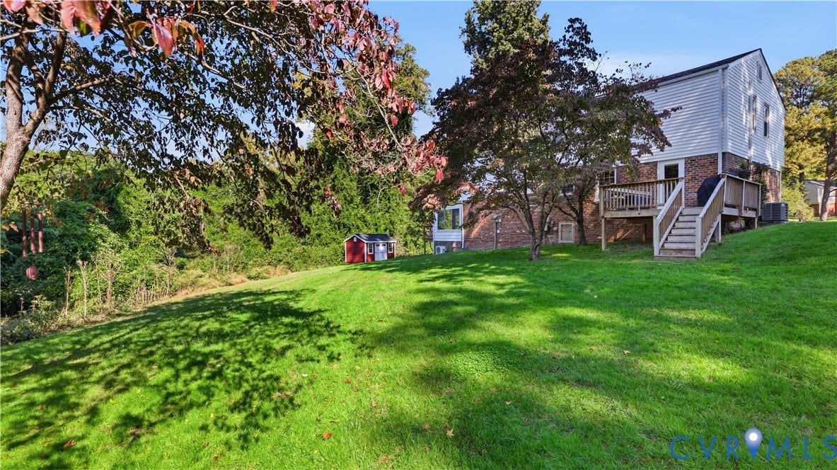 10010 Cheyenne Court, Richmond, VA 23235 Exterior featuring a brick and siding facade, raised wood deck with staircase, expansive sloped lawn, mature trees, and detached storage shed
