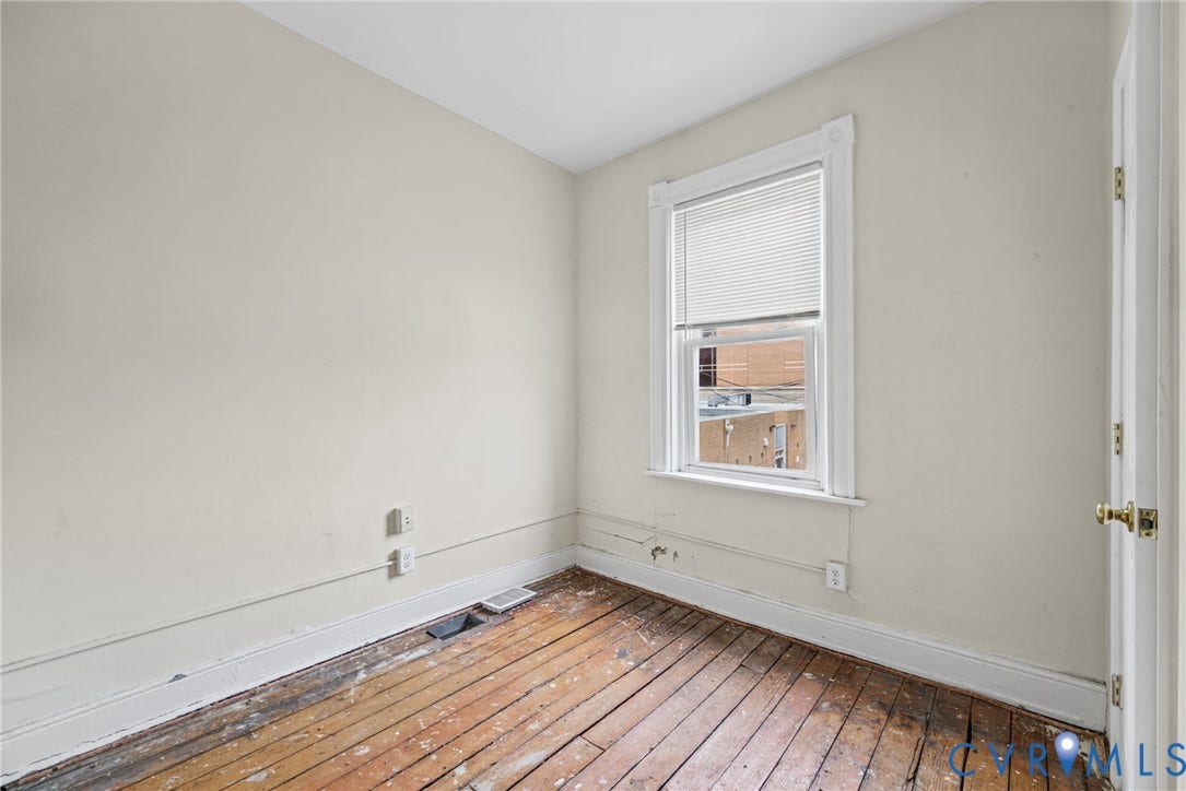 510 N 3rd Street, Jackson Ward, Richmond, VA 23219 Bedroom 3 - Interior room featuring original wood-plank flooring, a single-pane window with white wood trim, and a classic hinged door with brass-finish hardware