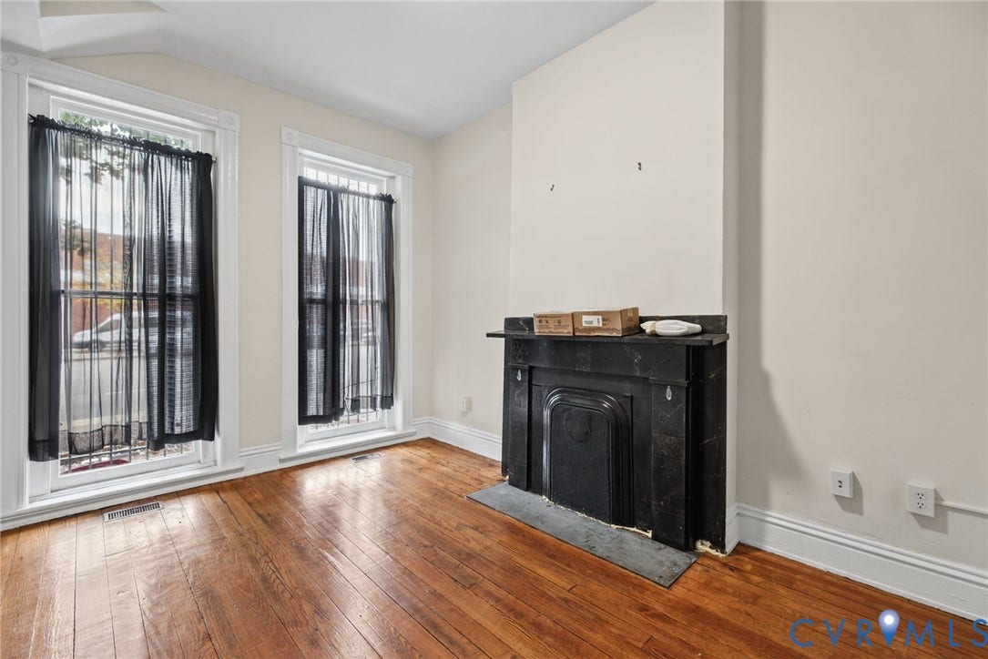510 N 3rd Street, Jackson Ward, Richmond, VA 23219 Interior space featuring hardwood flooring, two tall windows with decorative trim, and a dark stone fireplace mantel