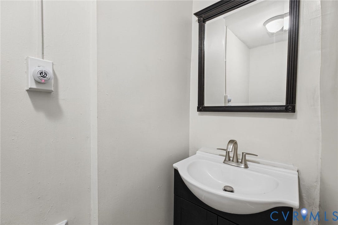 510 N 3rd Street, Jackson Ward, Richmond, VA 23219 Vanity featuring a dark-finish base cabinet, integrated white porcelain sink, and brushed metal dual-handle faucet, accented by a wall-mounted mirror with a dark frame and a dome-style overhead light fixture