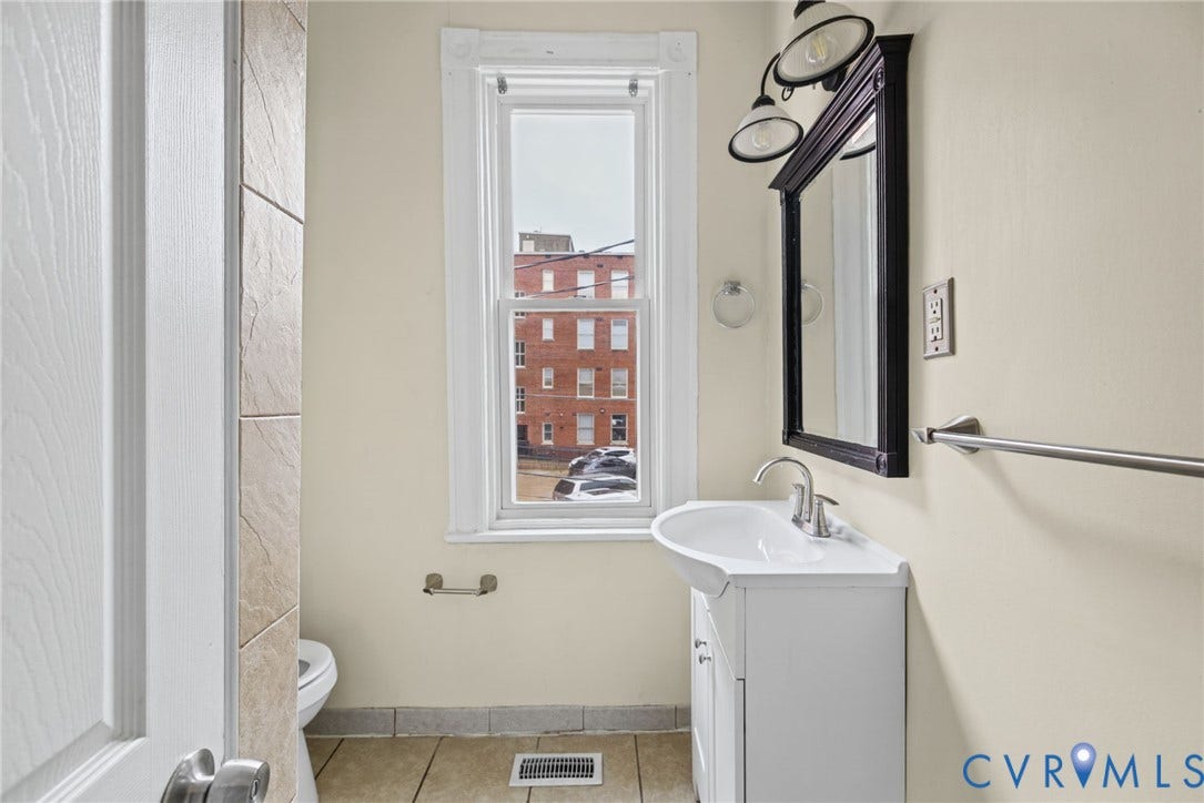 510 N 3rd Street, Jackson Ward, Richmond, VA 23219 White pedestal sink with a polished chrome faucet, framed dark-finish wall mirror, multi-light fixture, and ceramic tile flooring