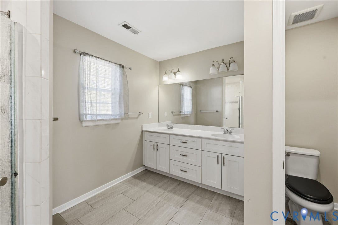 6614 Gills Gate Drive, Chesterfield, VA 23832 Double vanity with white cabinetry, solid surface countertop, tile flooring, and wall-mounted light fixtures