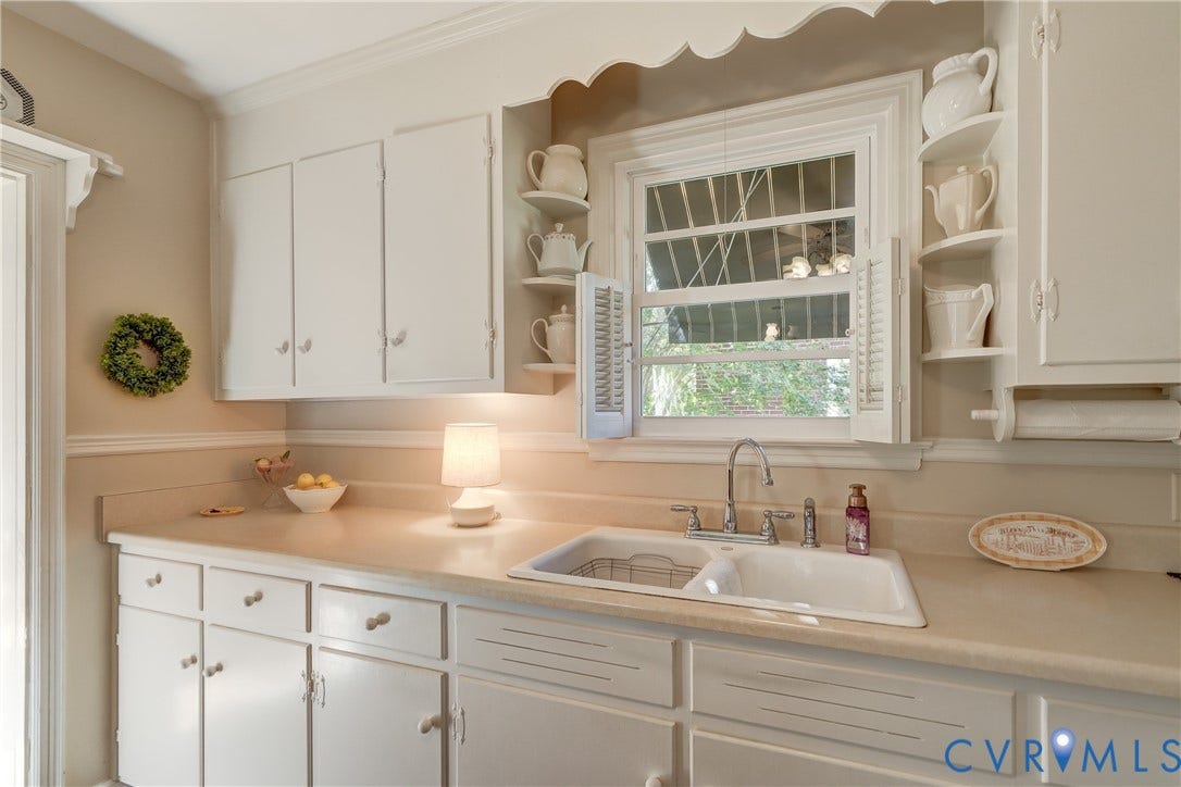 409 Lilliston Avenue, Colonial Heights, VA 23834 Kitchen featuring white cabinetry with integrated scalloped valance, solid-surface countertops, double-basin sink with metallic faucet, and decorative corner shelving