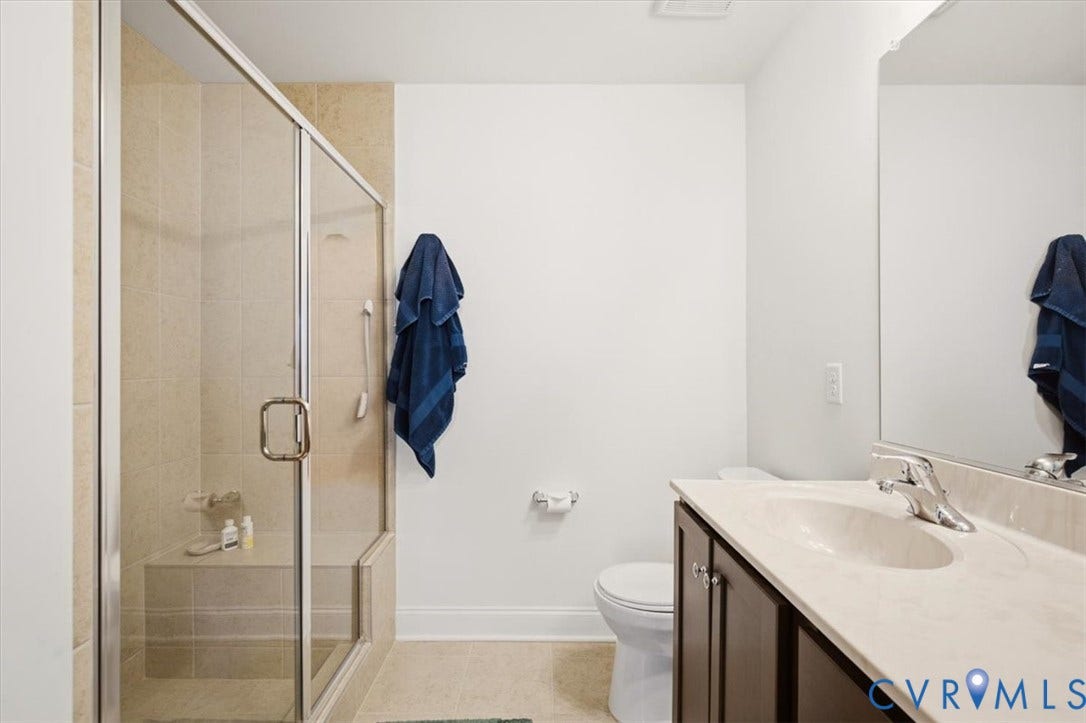 18743 Palisades Ridge, Palisades Cove, Moseley, VA 23120 Bathroom featuring a glass-enclosed shower with tile surround and integrated bench, dark wood-finish cabinetry, solid-surface countertop with integrated sink, and full-width wall mirror
