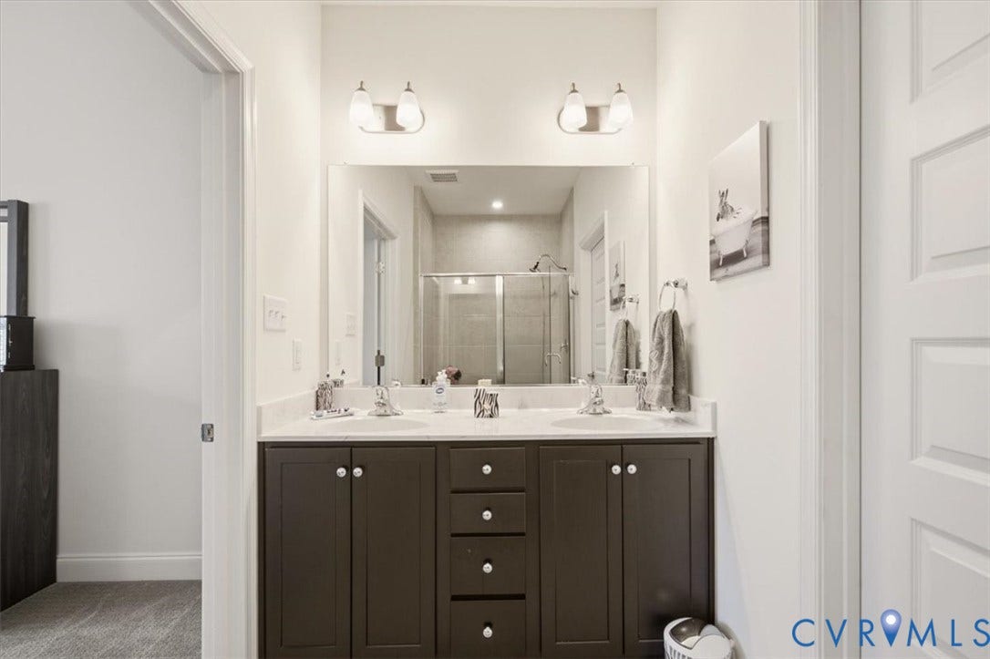 18743 Palisades Ridge, Palisades Cove, Moseley, VA 23120 Dark cabinetry vanity with a stone countertop, dual undermount sinks, two-light wall-mounted fixtures, and an oversized frameless mirror