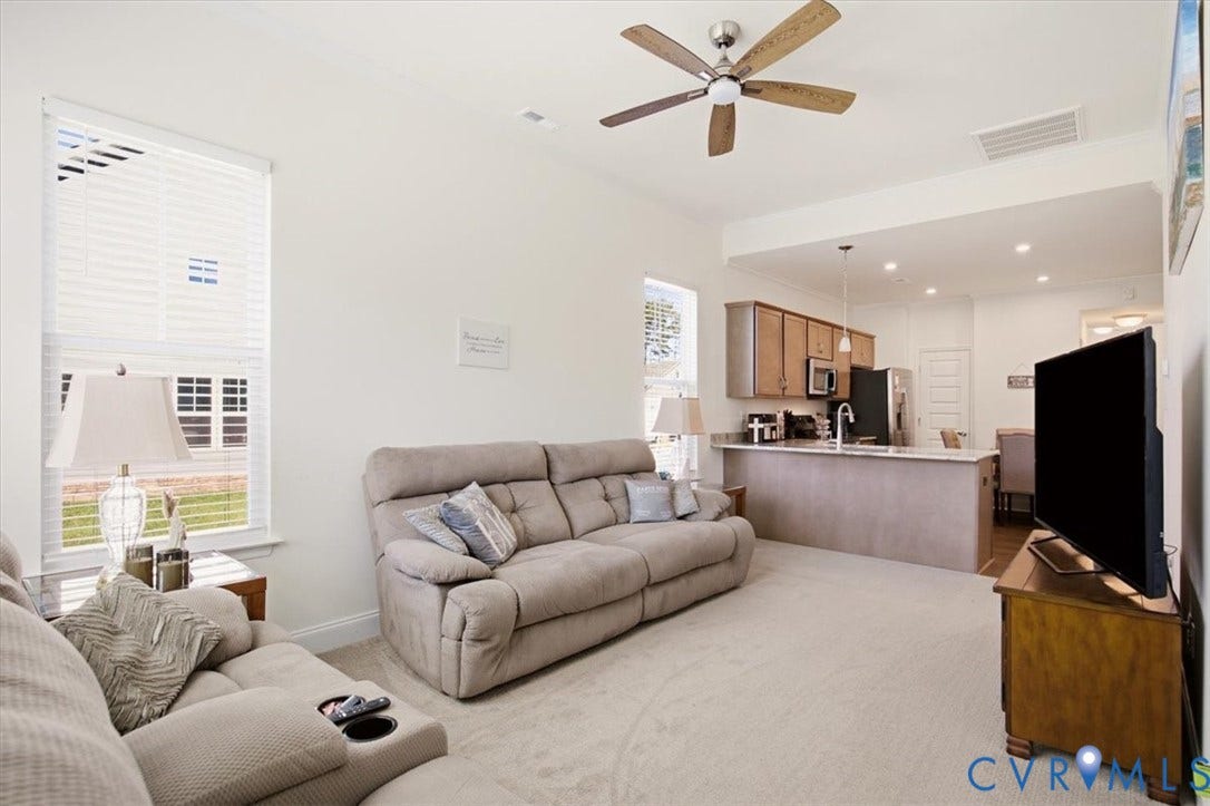 18743 Palisades Ridge, Palisades Cove, Moseley, VA 23120 Open-concept interior featuring a breakfast bar with stone-surface countertop, cabinetry with brushed-metal hardware, ceiling fan with light fixture, and windows with horizontal blinds