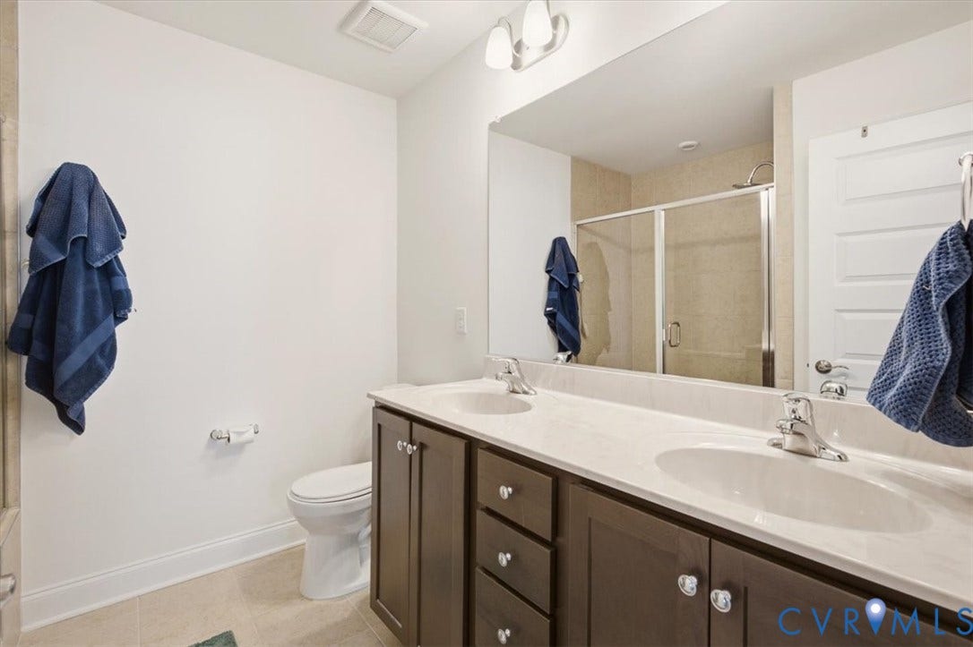 18743 Palisades Ridge, Palisades Cove, Moseley, VA 23120 Dual-sink vanity with dark wood-finish cabinetry, solid surface countertop, large wall-mounted mirror, and glass-enclosed shower