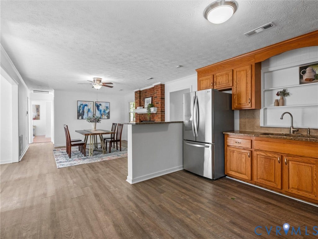 5504 Chanson Road, Salem Woods, North Chesterfield, VA 23237 Kitchen featuring wood cabinetry, stone countertops, stainless steel refrigerator, and integrated shelving, complemented by wood-finish flooring and a red brick fireplace
