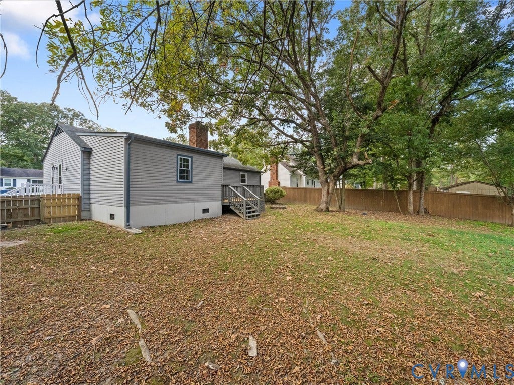 5504 Chanson Road, Salem Woods, North Chesterfield, VA 23237 Rear exterior featuring light-colored horizontal siding, a wood-frame deck with stairs, a brick chimney, and a full-perimeter privacy fence