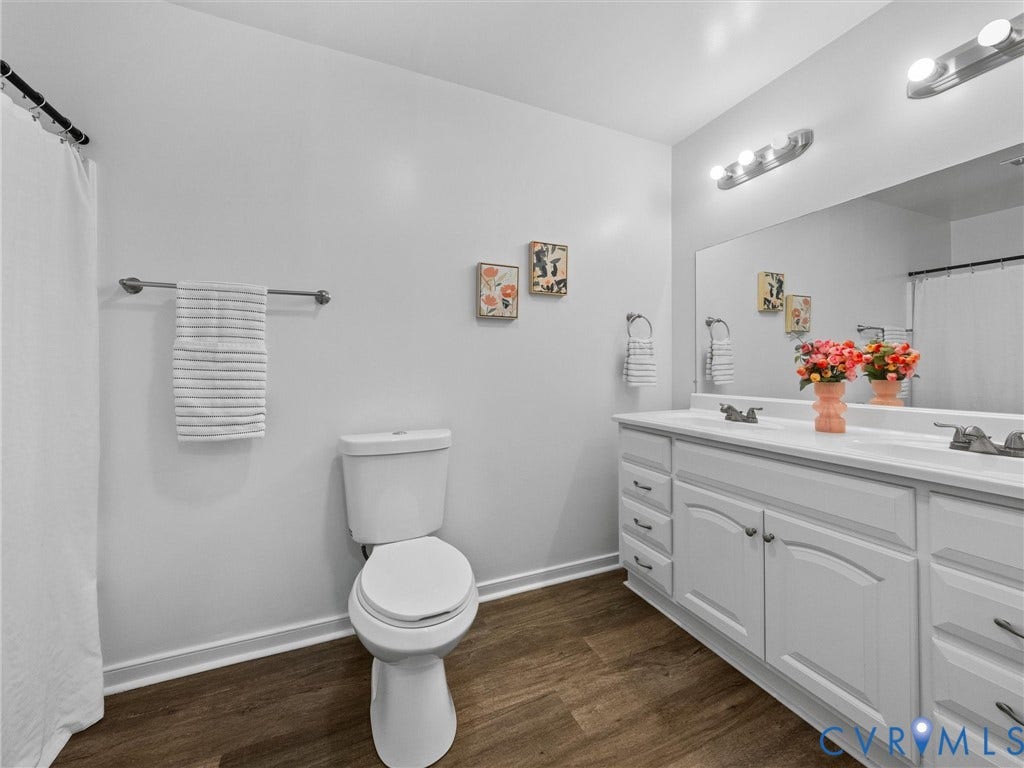 5504 Chanson Road, Salem Woods, North Chesterfield, VA 23237 Double-sink vanity with white cabinetry, wood-finish flooring, full-width wall mirror, and dual multi-bulb vanity light fixtures