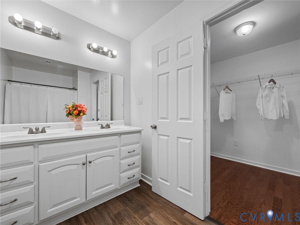 5504 Chanson Road, Salem Woods, North Chesterfield, VA 23237 Dual-sink vanity with white cabinetry and expansive wall-mounted mirror, brushed-nickel lighting fixtures, six-panel interior door, and wood-finish flooring