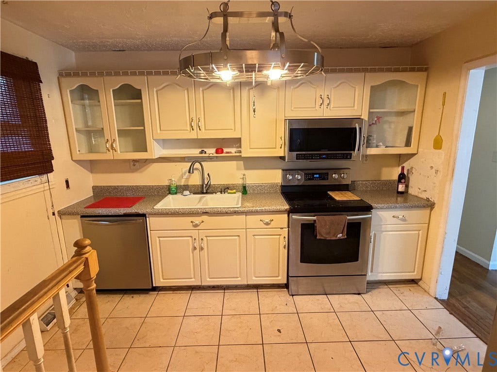 1513 West Lane, Petersburg, VA 23803 Kitchen featuring off-white cabinetry with glass-paneled uppers, stainless steel appliances, a double-basin sink, stone-finish countertops, and a decorative metal-frame overhead light fixture