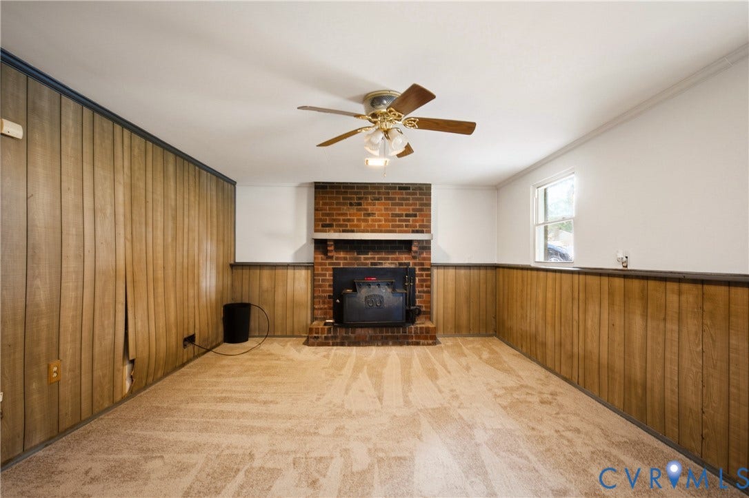 Floor-to-ceiling wood paneling, red brick fireplace, wood-burning stove insert, and a ceiling-mounted light fixture with a fan