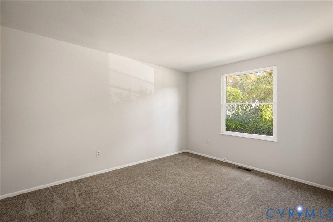 Neutral-toned interior featuring wall-to-wall carpeting and a single-pane window with external foliage