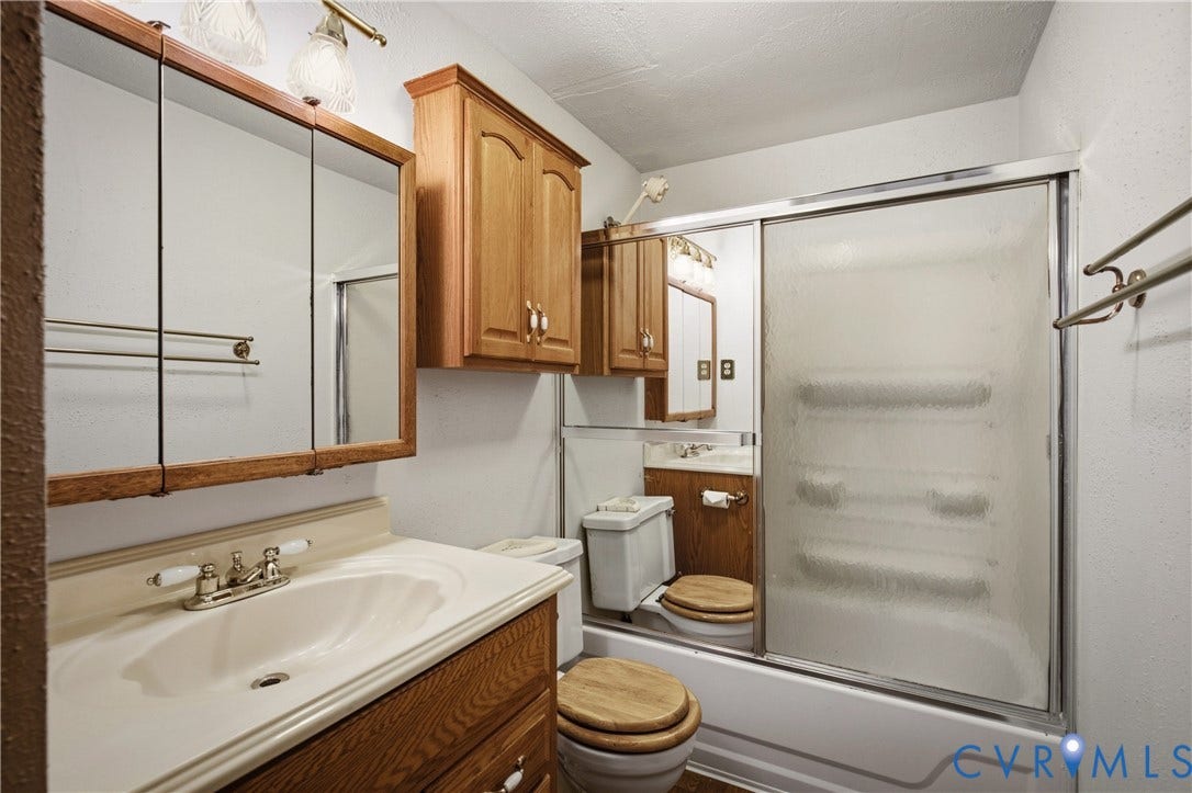 Bathroom featuring a wooden vanity with integrated sink, tri-fold medicine cabinet, wood-finish cabinetry, and a tub-shower combination with sliding glass doors