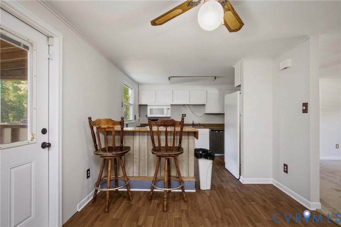 Kitchen featuring a breakfast bar with wood-finish paneling, white cabinetry, integrated microwave, ceiling fan with light fixture, and wood-finish flooring