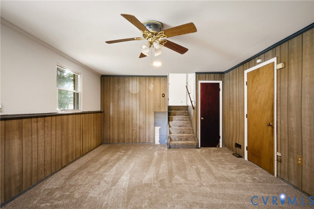 Wood-panel wall cladding, ceiling fan with integrated light fixture, neutral wall-to-wall carpeting, and interior solid-core doors