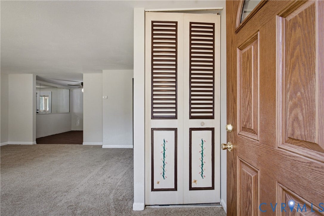Entryway featuring a wood-finish front door with a half-moon light, bi-fold closet doors with louvered panels, and wall-to-wall carpeting