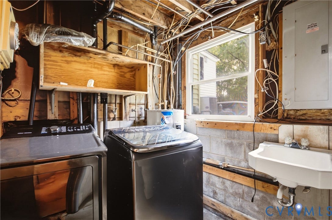 Utility area featuring a wall-mounted basin, single-hung window, exposed timber framing, and electrical service panel